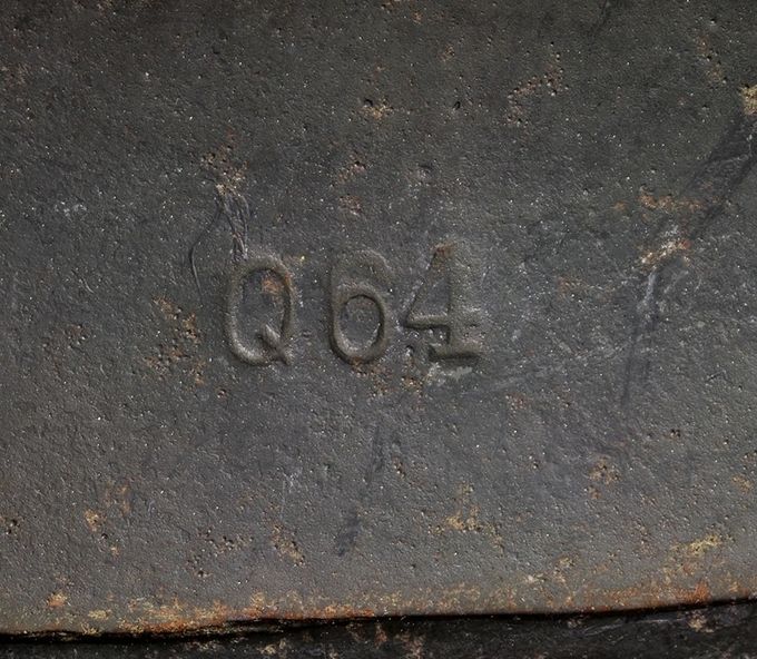 Produsentmerking av Quist fabrikken, Q64. Tallet 64 betyr antall cm rundt kanten på stålskallet. Dette kan variere fra 60 til 70 cm.