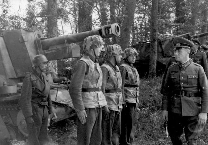 Feltmarskalk Erwin Rommel inspiserer en artillerienhet i 21. Pz. Divisjon. Soldatene har den samme kamuflasjebånd konfigurasjonen på hjelmene sine. Tekstilet på båndene har forskjellige farger og tekstur.